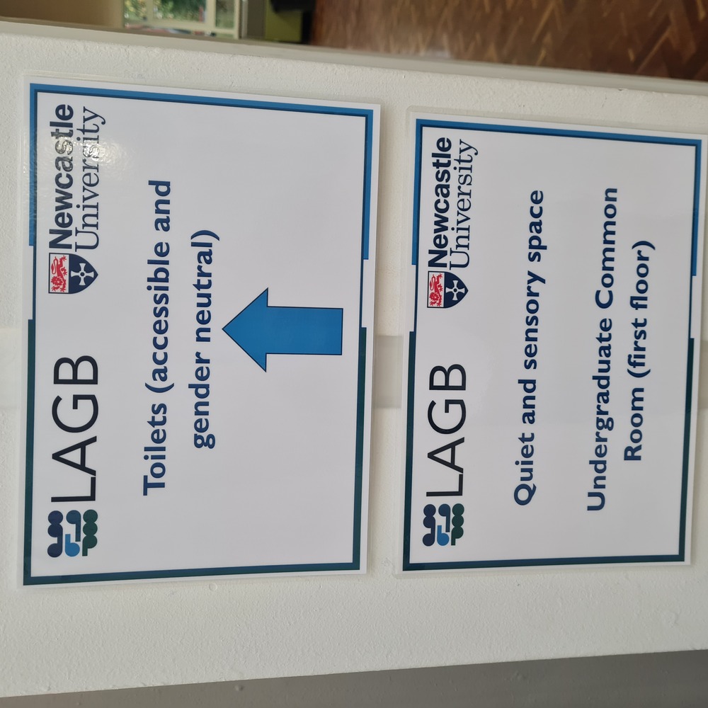 Two signs. The first has an upwards arrow and the text "Toilets (accessible and gender neutral)". The second has the text "Quiet and sensory space. Undergraduate common room (first floor)"
